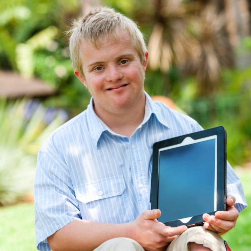 Close up portrait of disabled boy holding blank tablet with copy space outdoors.